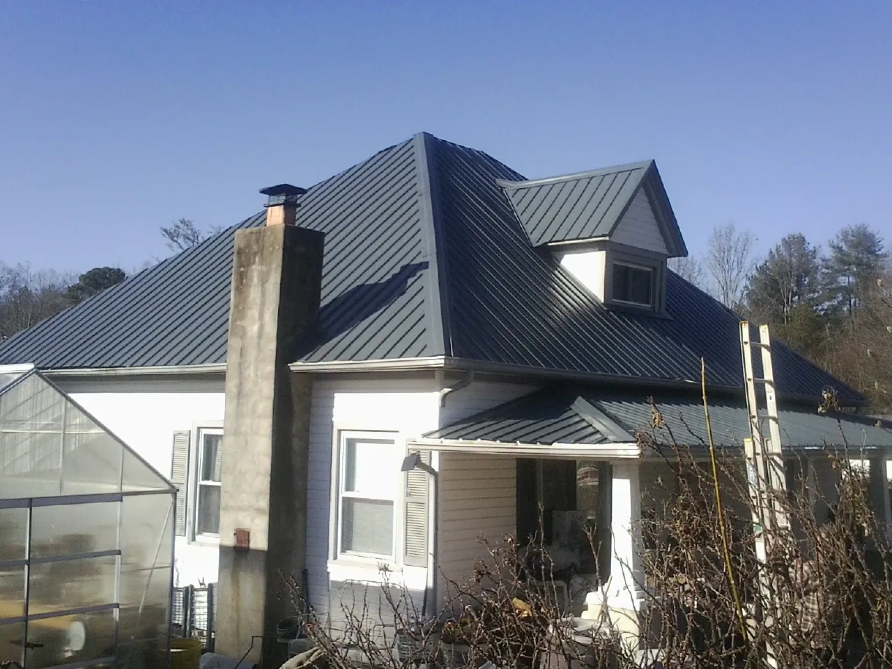 Dark blue standing seam metal roof on a white farmhouse with dormer — Slate & Tile Roof Repair by Roofing Brothers in Colquitt