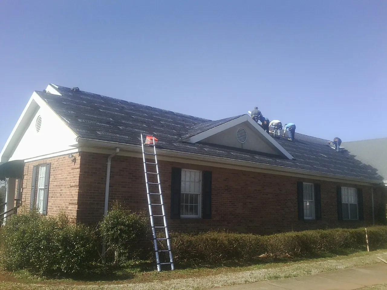 Crew tearing shingles off a brick ranch roof with a ladder set — Emergency Roof Repair work by our crew in Colquitt