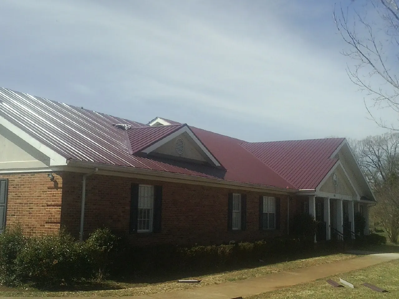 Red metal roof with gabled entries on a long brick building, from a Hail Damage Roof Repair job in Colquitt