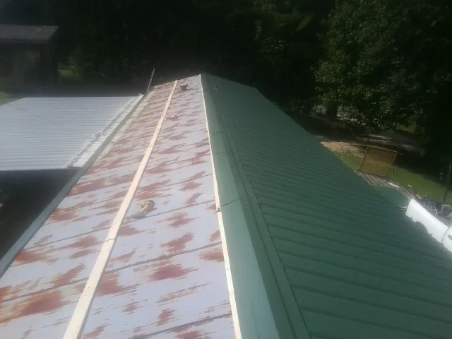 Old rusted panels beside newly installed green metal roofing — Wind Damage Roof Repair by Roofing Brothers in Colquitt