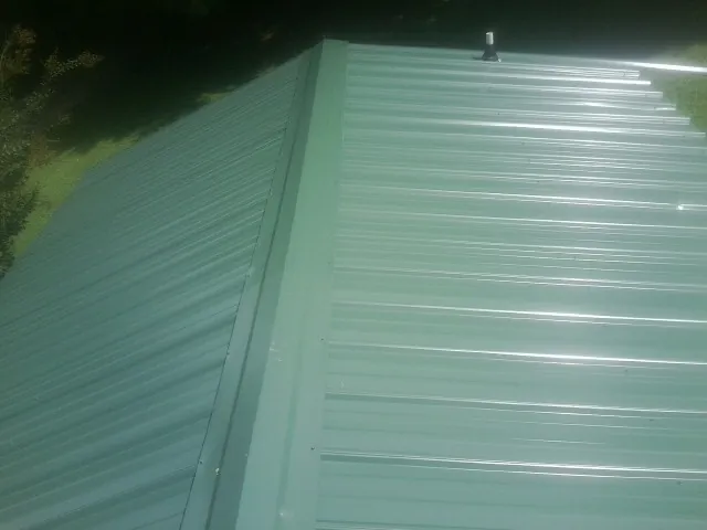 New green metal panels meeting at the ridge of a roof — Flat Roof Repair work by our crew in Colquitt