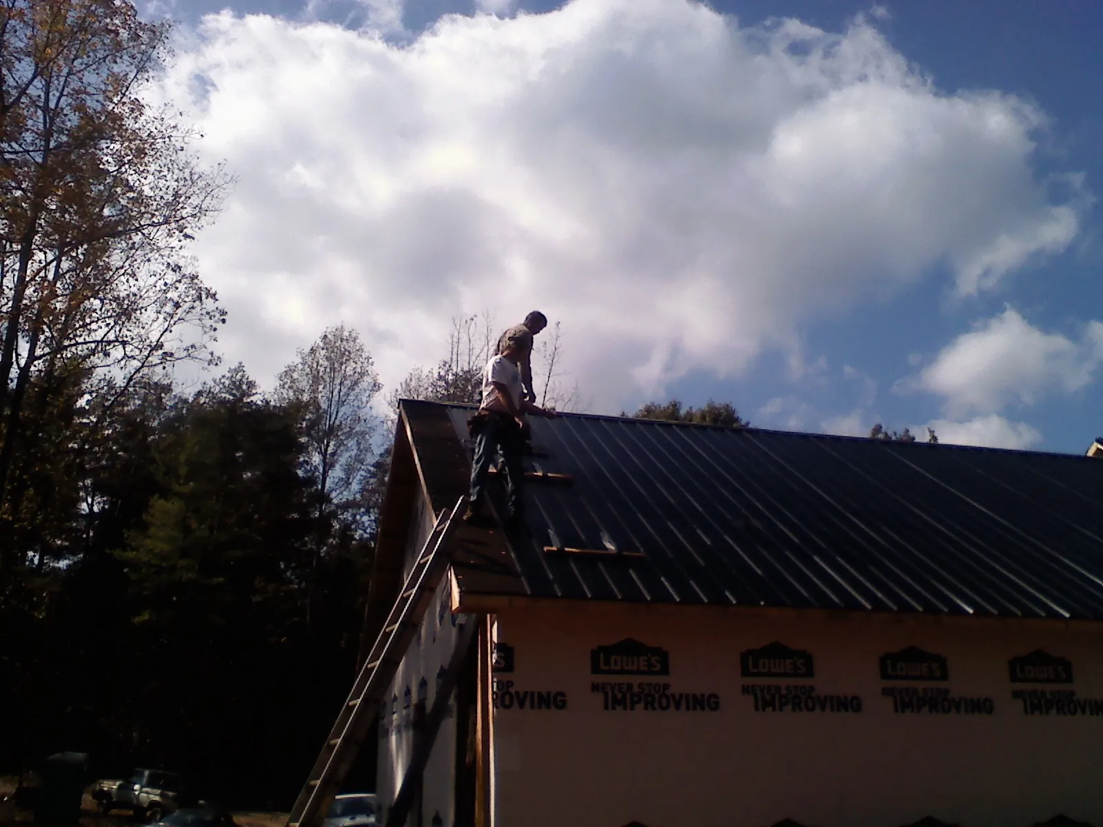 Roofer fastening dark metal panels high against a cloudy sky, from a Roof Inspection job in Colquitt